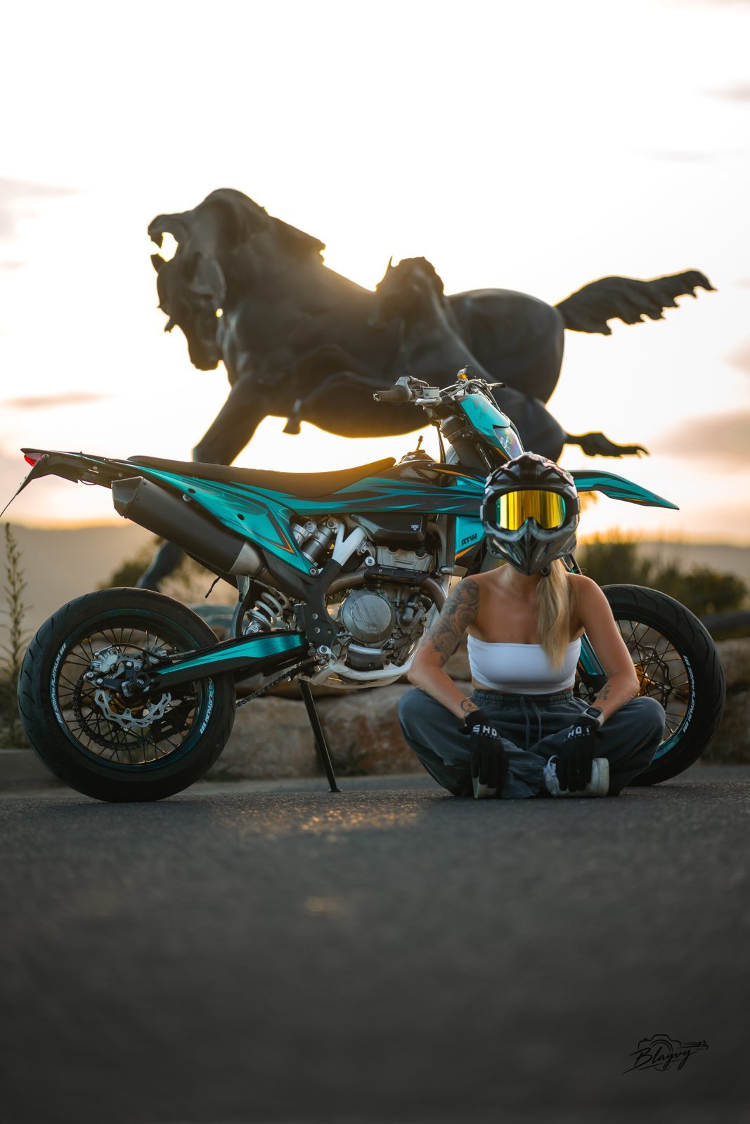 Assise en tailleur devant la moto et la statue au coucher du soleil